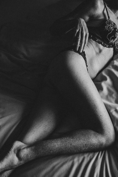 Künstlerische Schwarz-Weiß-Aufnahme einer Frau in schwarzer Lingerie auf einem Bett mit intensivem Licht-und-Schatten-Spiel.