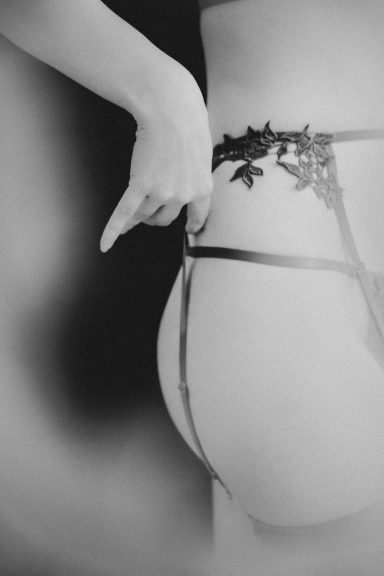 Schwarz-Weiß-Detailaufnahme von Lingerie mit feinen Bändern und einer Hand am Körper.