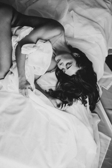 Schwarz-Weiß-Boudoir-Aufnahme einer Frau, die auf weißen Laken liegt.