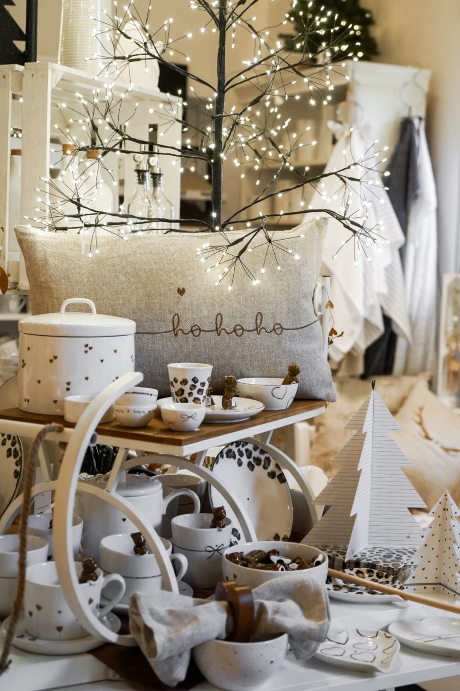 Weihnachtliche Produktpräsentation mit leuchtendem Dekobaum, Keramik und Kissen mit Ho-ho-ho-Schriftzug.
