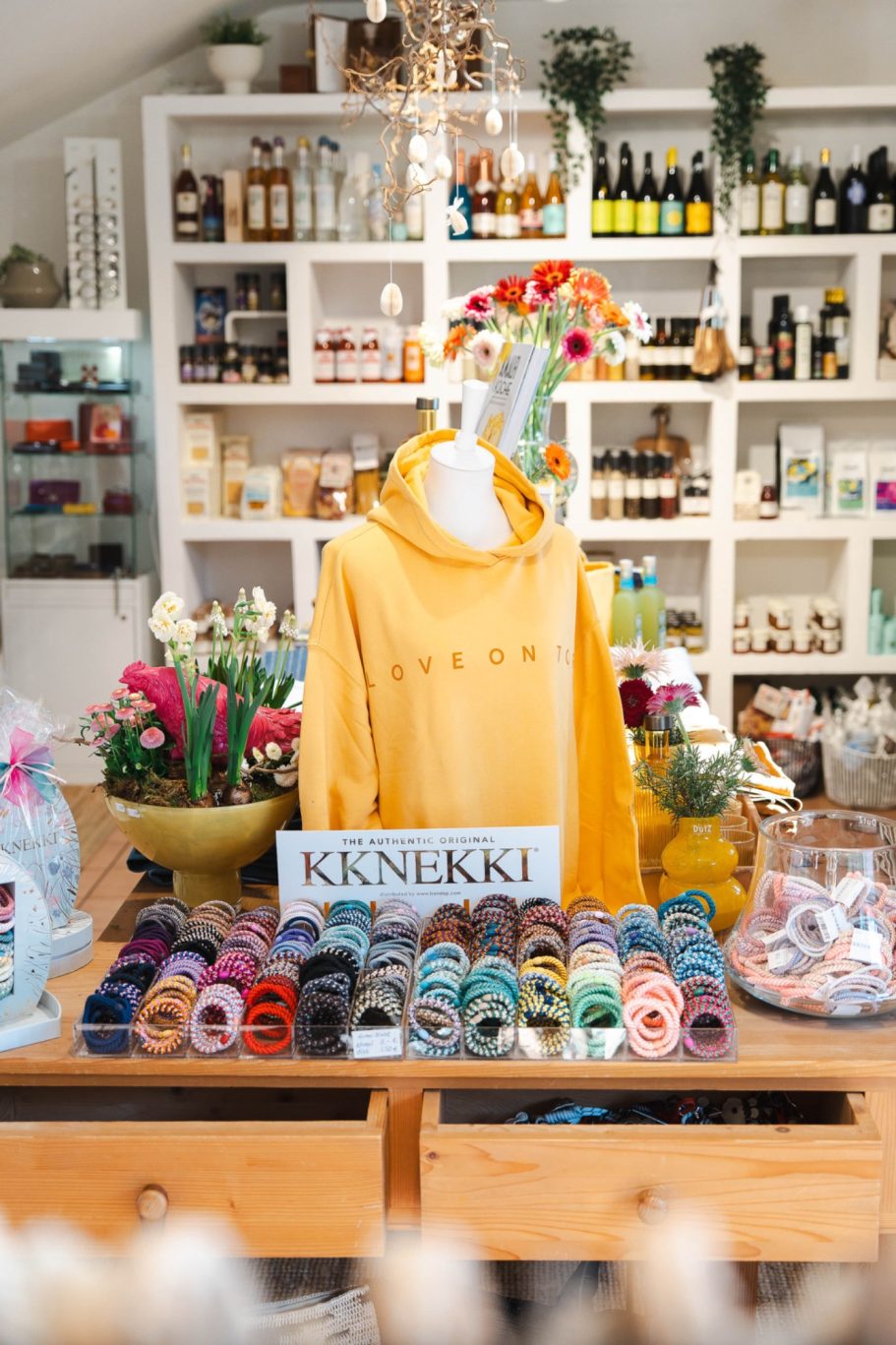 Farbenfrohe Produktpräsentation im Concept Store mit gelbem Hoodie, Blumen und KKNEKKI Haargummis.