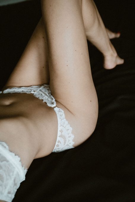 Sanfte Detailaufnahme einer Frau in weißer Spitzenwäsche mit Fokus auf Körperformen und natürlichem Licht.