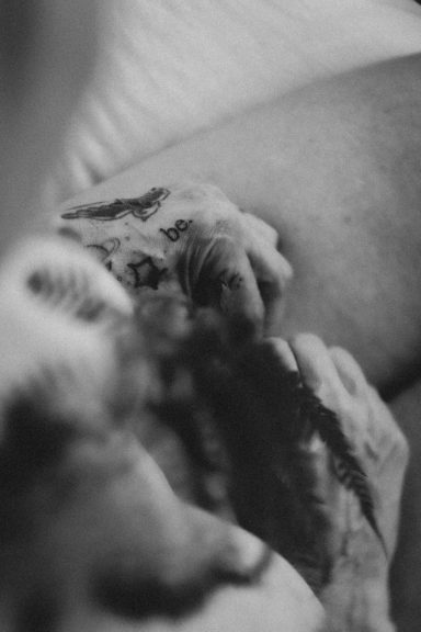 Schwarz-Weiß-Detailaufnahme einer tätowierten Hand und eines Farnzweigs auf einem weiblichen Körper