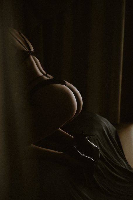 Stimmungvolle Detailaufnahme einer Frau in schwarzer Lingerie und High Heels bei tiefem, weichem Licht.