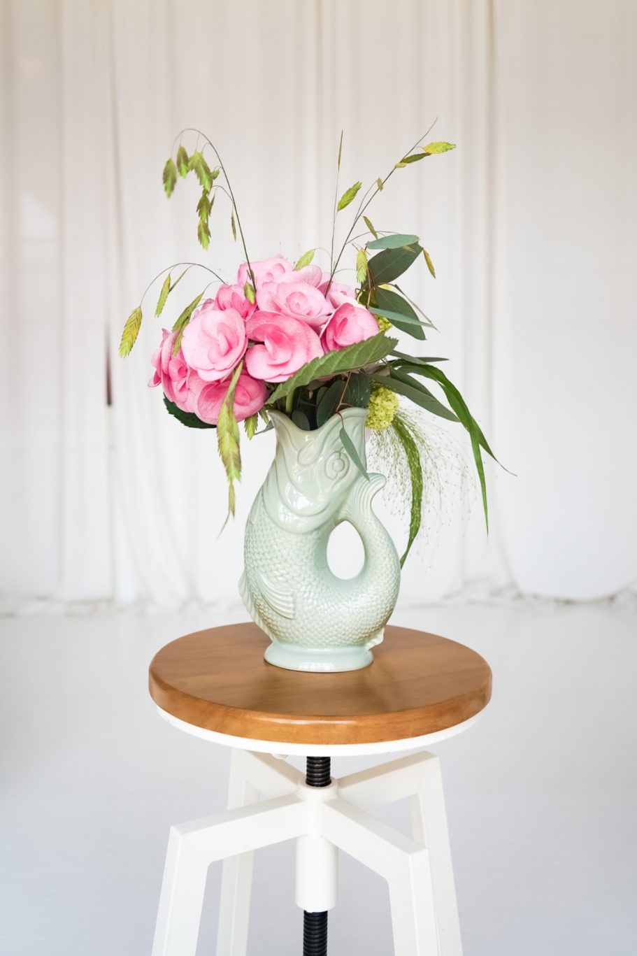 Rosa Hortensien und feine Gräser in einer hellgrünen Keramikvase in Fischform.