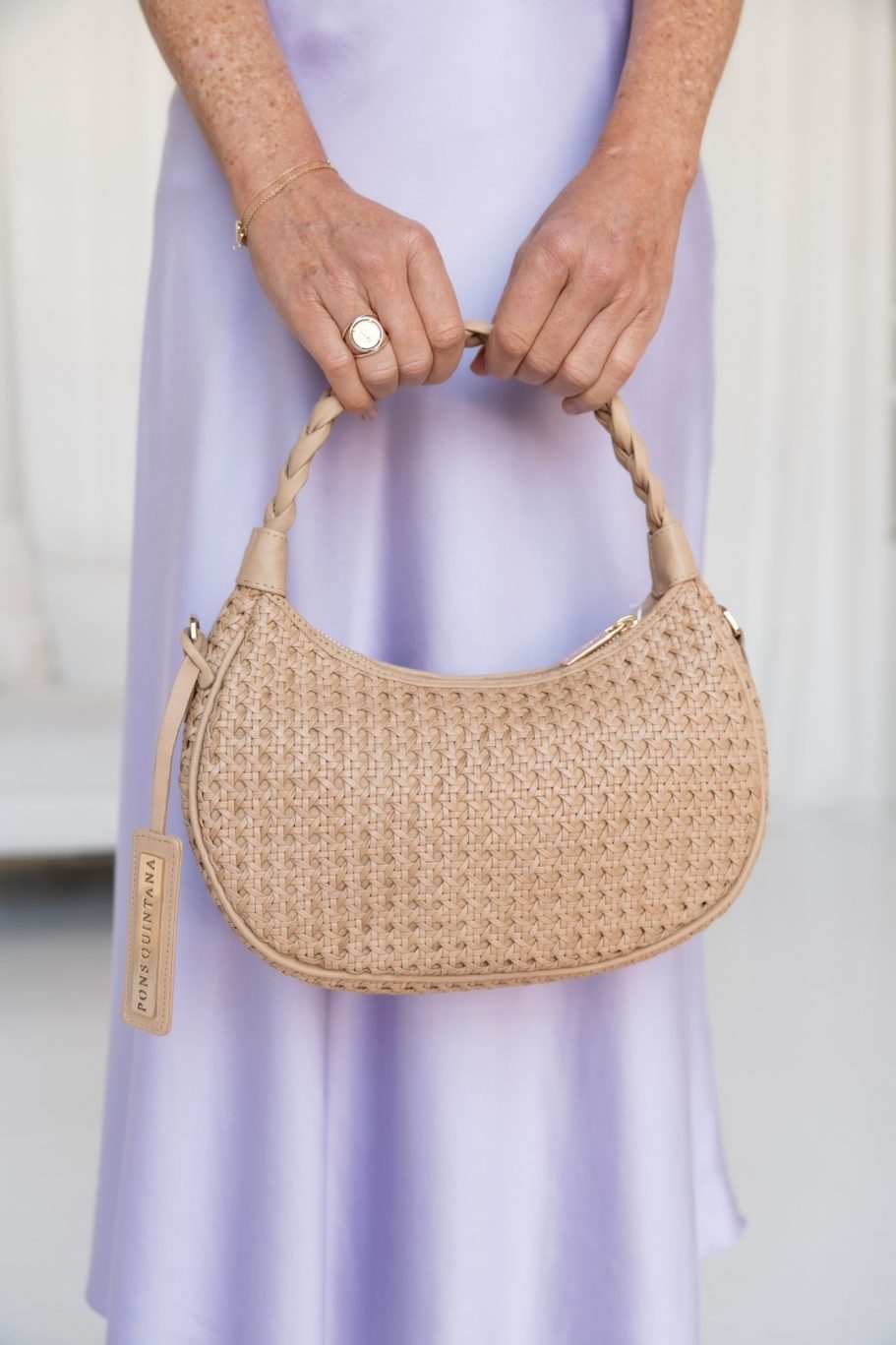 Beige geflochtene Handtasche von Pons Quintana, gehalten vor einem fliederfarbenen Kleid.