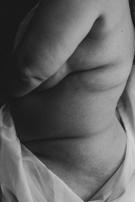 Detailaufnahme eines kurvigen weiblichen Körpers mit natürlichen Hautfalten in kontrastreicher Schwarz-Weiß-Fotografie