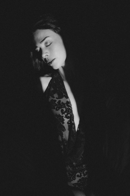 Ausdrucksstarkes Schwarz-Weiß-Boudoir-Porträt einer Frau im schwarzen Spitzenbody im Spiel von Licht und Schatten.