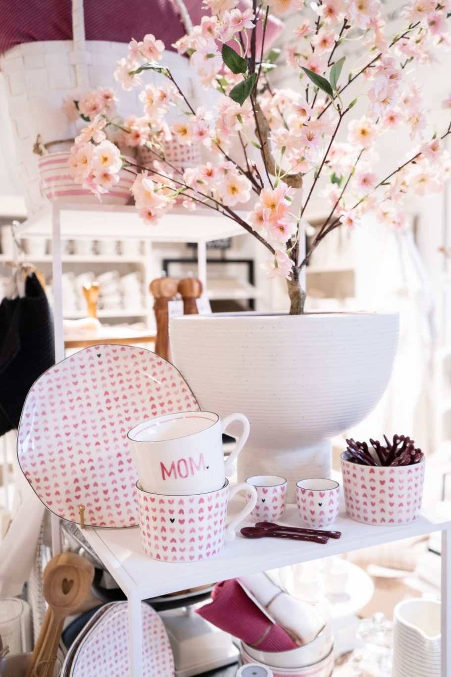 Frühlingshafte Warenpräsentation mit rosa Herzgeschirr und blühenden Zweigen in einer großen weißen Vase.