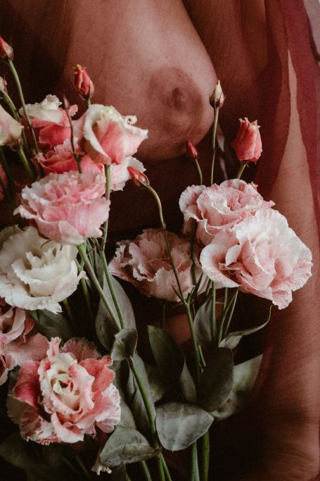 Künstlerische Aufnahme eines weiblichen Körpers mit rosa und weißen Blumen.