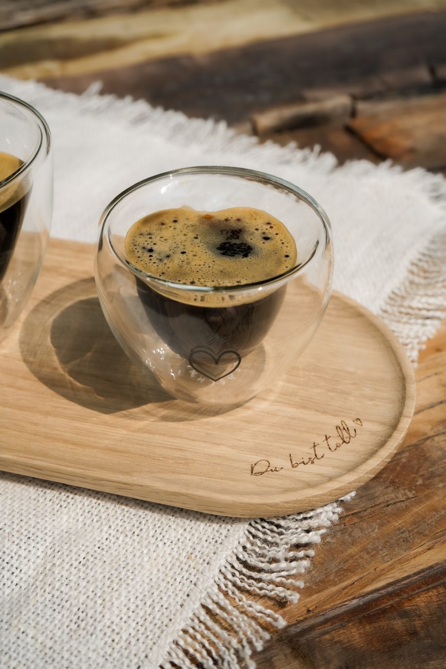 Espresso im doppelwandigen Herzglas auf einem Holztablett mit eingraviertem Schriftzug Du bist toll.
