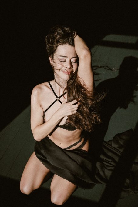 Frau in schwarzer Lingerie kniet mit geschlossenen Augen im dramatischen Licht-und-Schatten-Spiel.